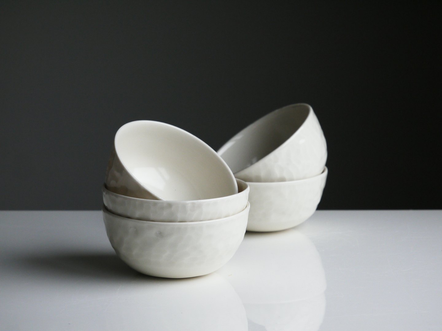 Two stacks of hammered white ceramic bowls on a reflective surface.